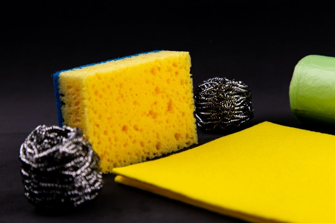 Cleaning supplies including a sponge, cloth, and scrubbers on a dark surface.